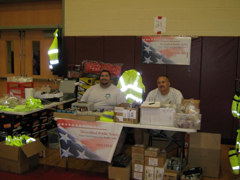 2 men sitting at a table with uniforms and other various public safety equipment